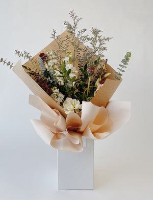Wild textured bouquet with baby blue eucalpytus, limonium filler, anemone and scabiosa in an upright delivery box wrapped in kraft paper