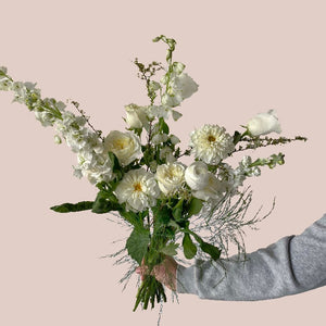 A botanical handtied flower arrangement with white roses, white mums and white delphinium