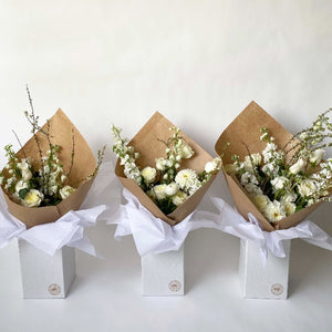 Three sizes of botanical handtied flower arrangement with white roses, white mums and white delphinium displayed in upright delivery box